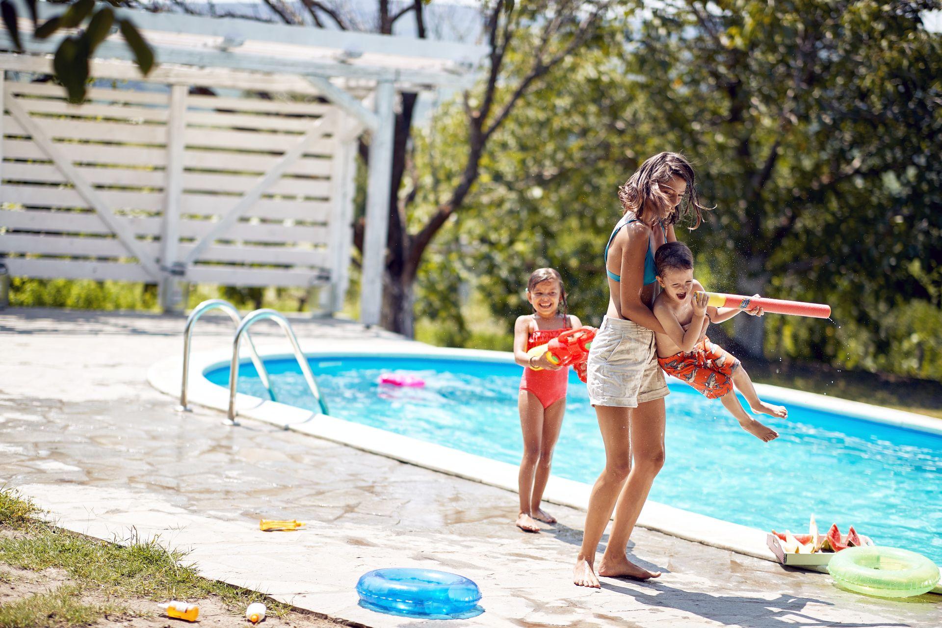 Mutter spielt mit Kindern am Poolrand, Wasserspielzeug und Obst im Familiengarten